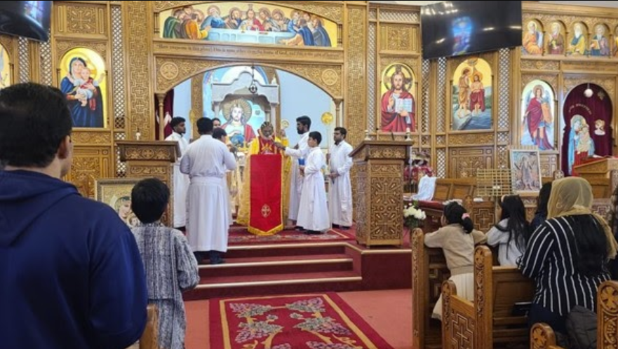 Holy Mass celebration in Malankara Catholic Church with ornate iconostasis, clergy in white vestments, and congregation