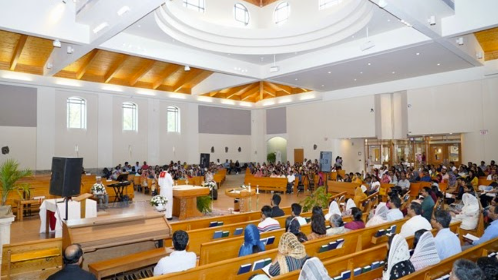 Large congregation gathered in beautiful modern church sanctuary during annual summer retreat with vaulted wooden ceiling and professional sound setup
